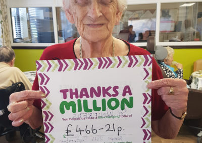 A smiling female resident at St Winifreds Care Home holding up a Macmillan poster showing £466.21 total