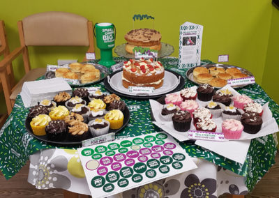 An impressive cake table display at St Winifreds Care Home with Macmillan Cancer Support stickers and signs